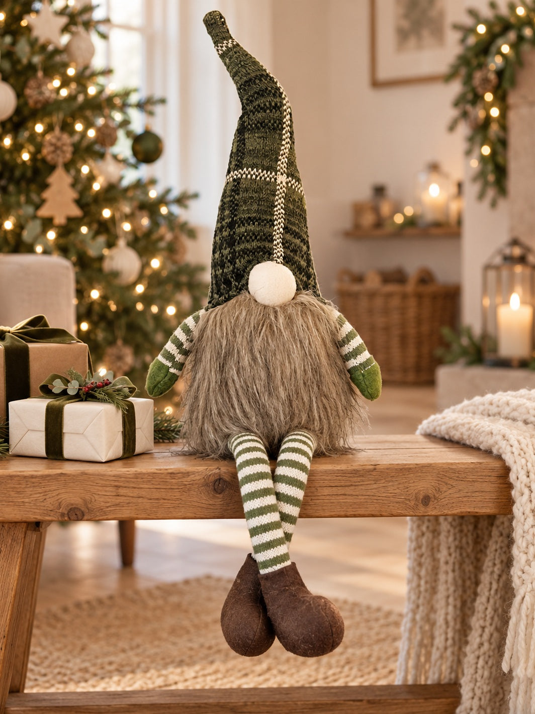 A Christmas gnome doll sits on a wooden bench in a cozy living room setting. The gnome has a tall dark green and cream knit hat, a shaggy brown beard, green and cream striped sleeves and legs, and brown felt shoes.